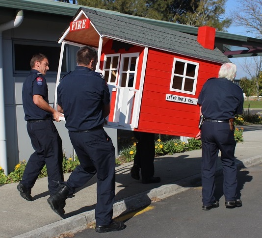 FIRE SERVICE: Hamilton Fire Fighters carry the playhouse in to the community centre.  Photo: Shontelle Cargill