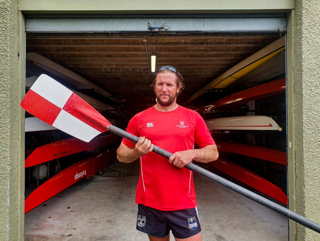 Shane Quintus holding a paddle while standing in front of the Hamilton Rowing Club's boat shed.